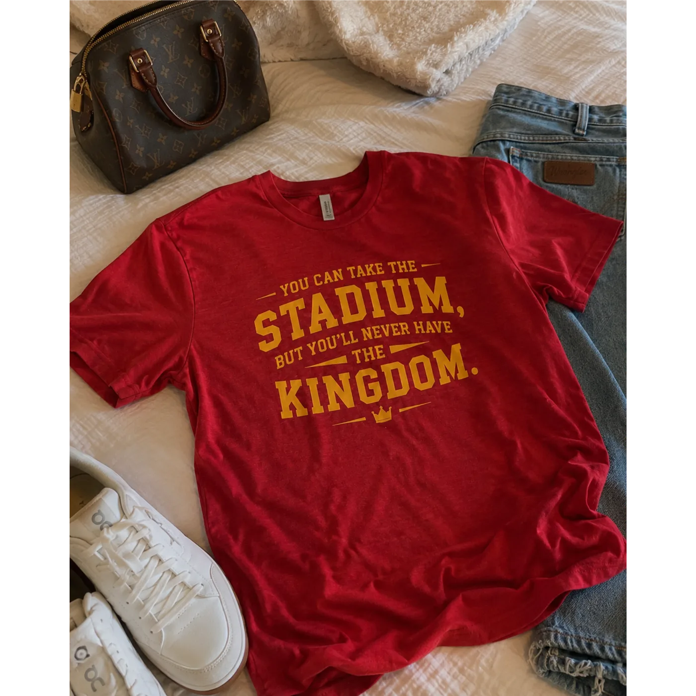 The red Kingdom Tee styled with jeans, white sneakers, and a handbag